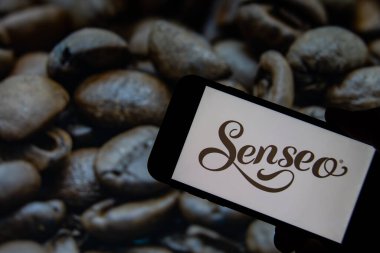 Rheinbach, Almanya 1 Ekim 2021, Senseo 'nun marka logosu kavrulmuş kahve çekirdekli bir resmin önünde bir akıllı telefonun önünde sergilenmektedir (marka logosuna odaklan)
