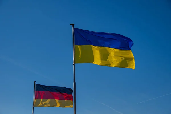 The Ukrainian flag and a German flag wave against a cloudless sky