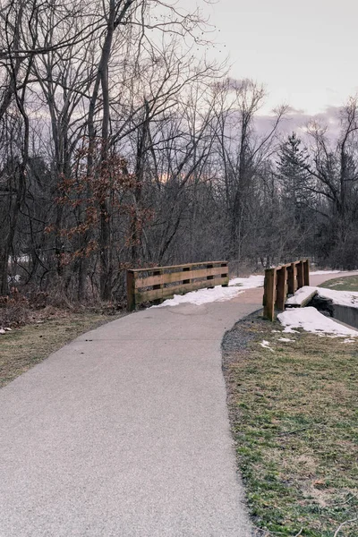 夕暮れ時に小さな木製の橋と雪のある公園の道冬や日没に向かう人生の概念的なパス — ストック写真