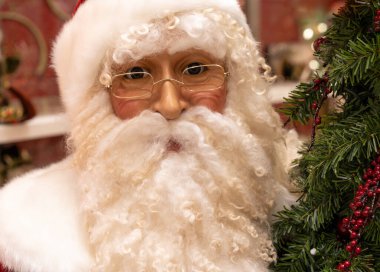 Las Vegas, NV - Dec. 12, 2021: Life size Santa Claus display doll beside a Christmas tree, close up of face with wire rim glasses