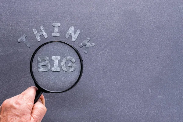 Think Big concept with chalkboard background and hand holding mangnifying glass over galvanized letters