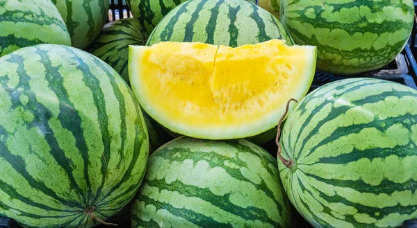 fresh yellow water melon cut open on top of a pile of green melons at the farmers market