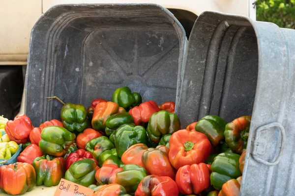 red and green bell peppers spilling out of two galvanized metal washtubs on a table at the farmers market