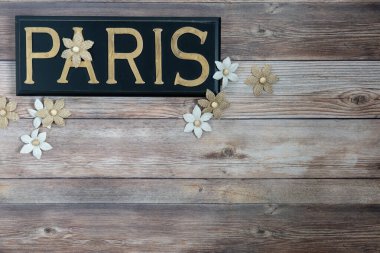 Paris kelimesi siyah boyalı ahşap üzerine pirinç harflerle eski ahşap arka planda çuval çiçekleri.