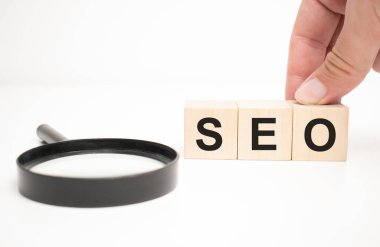 seo text ahşap küp bloklar ve masa arkasında el ele büyüteç.