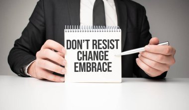 Bir adam gümüş bir kalem ve el sıkışma kartıyla not defterine yazar. Değişikliğe karşı koyma. Gri arka plan, ön manzara. işletme ve eğitim kavramı.