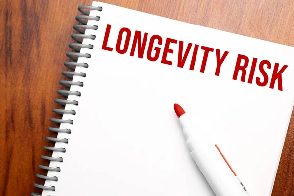 Text LONGEVITY RISK written in notepad, Office wood table from above, concept image for blog title or header image. Aged vintage color look.