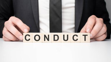 Tahta bloğu tutan bir iş adamı. İş adamı, tahta küplere CONDUCT yazısıyla bakıyor. Finansal. finansman