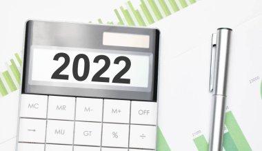 İş ve finans kavramı. Masanın üzerinde bir kalem ve hesap makinesi var. Metin 2022 'de yazılmış.