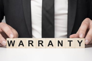 Tahta bloğu tutan bir iş adamı. İşadamı, tahta küplere WARRANTY yazısıyla bakıyor. Finansal. finansman