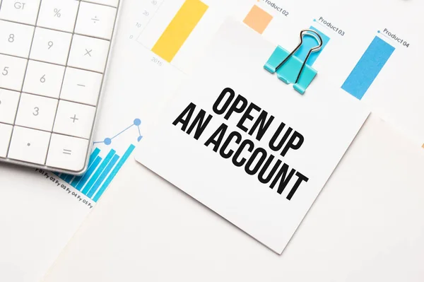 OPEN UP AN ACCOUNT text concept. Office workplace table with calculator, graphs, reports and the text Budget 2021 on a small piece of paper on multicolored background.