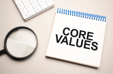 İş ve finans kavramı. Masanın üzerinde bir büyüteç, bir hesap makinesi ve içinde Ana Değerler yazan bir defter var.