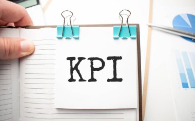 Beyaz gelecekteki hesap makinesi, kağıt çarşaf, pembe ataç ve gümüş renkli kalem. KPI Metni