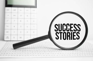 Hesap makinesiyle beyaz masada metin başarı hikayeleri içeren büyüteç