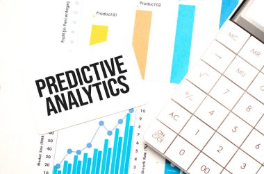 Hesap makinesi, grafikler, raporlar ve çok renkli arkaplan üzerine küçük bir kağıt parçası üzerinde PredICVE ANALYTICS metni içeren ofis çalışma masası.
