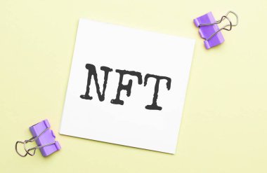 Kırtasiyeli sarı arkaplan üzerinde NFT metni olan beyaz kağıt