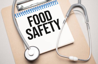 Üzerinde yiyecek güvenliği ve mavi arka planda steteskop yazan beyaz bir not defteri. Tıbbi konsept