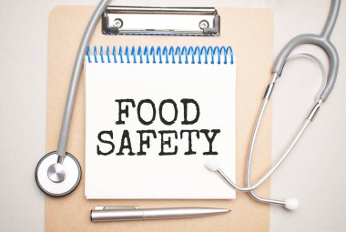 Üzerinde yiyecek güvenliği ve mavi arka planda steteskop yazan beyaz bir not defteri. Tıbbi konsept