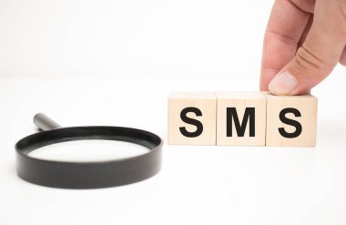 sms metin ahşap küp bloklar ve masa arkasında el ele büyüteç.