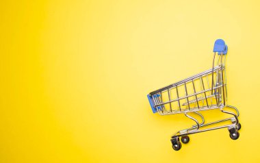 Sarı arka plandaki alışveriş arabasının fotokopi alanı ile yakın plan görüntüsü.