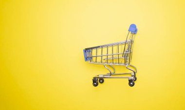 Sarı arka plandaki alışveriş arabasının fotokopi alanı ile yakın plan görüntüsü.