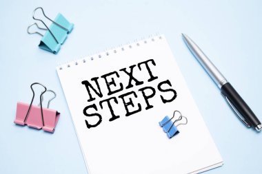 Mavi arkaplan üzerinde NEXT STEPS metin ve ofis araçları ile beyaz not defteri