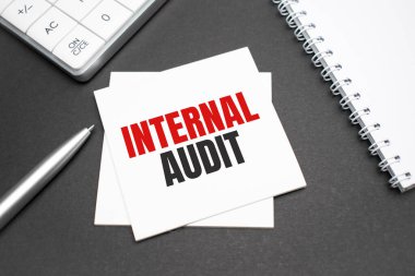 Hesap makinesi, kalem ve açık defter. Ahşap zemin üzerinde INTERNAL AUDIT ile yazılmış. İş Konsepti.