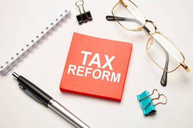 Masaüstünde raporlar, not defterleri, bir hesap makinesi, bir nakit para ve üzerinde TAX REform yazan kırmızı bir çıkartma var. İş konsepti
