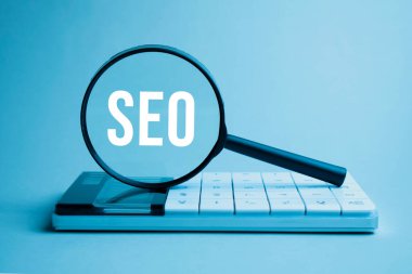 Finans ve iş konsepti. Beyaz arkaplanda bir hesap makinesi ve üzerinde SEO yazan bir büyüteç bulunur.