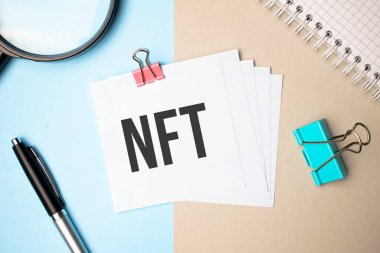 Hafif arka plan büyüteci, kalem ve NFT yazılı bir defter üzerinde. İş konsepti
