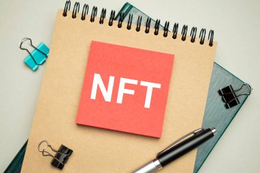 Masaüstünde raporlar, not defterleri, hesap makinesi, nakit para ve NFT yazılı sarı bir çıkartma var. İş konsepti
