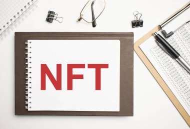 Masaüstünde raporlar, not defterleri, hesap makinesi, nakit para ve NFT yazılı sarı bir çıkartma var. İş konsepti