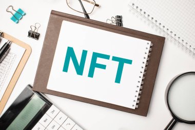 Masaüstünde raporlar, not defterleri, hesap makinesi, nakit para ve NFT yazılı sarı bir çıkartma var. İş konsepti