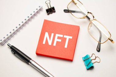 Masaüstünde raporlar, not defterleri, hesap makinesi, nakit para ve NFT yazılı kırmızı etiket var. İş konsepti