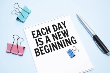 Mavi arkaplanda her gün yeni bir başlangıç ve ofis araçları içeren beyaz not defteri