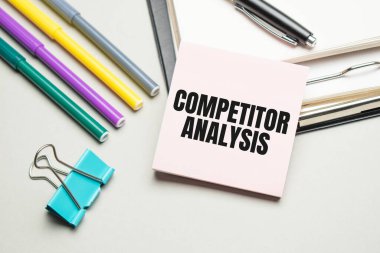 Raporlar ve renk çizelgeleri masada. Ayrıca siyah çerçevede kırmızı kalemler, kalemler ve kâğıtlar var. Üzerinde COMPETITOR ANALYSIS yazıyor. Yukarıdan görüntüle
