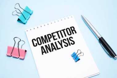 Metin COMPETITOR ANALYSIS ve mavi arkaplanda ofis araçları içeren beyaz not defteri