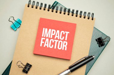 Masaüstünde raporlar, not defterleri, hesap makinesi, nakit para ve IMPACT FACTOR yazılı sarı bir çıkartma var. İş konsepti