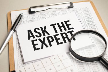 Masada raporlar, bir büyüteç, bir hesap makinesi ve üzerinde Uzmana Sor yazan beyaz bir not defteri var. İş konsepti