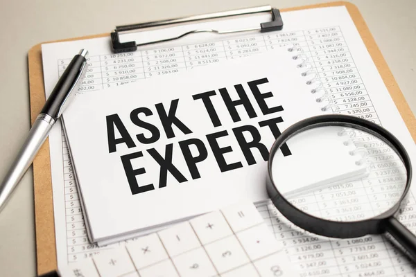 Masada raporlar, bir büyüteç, bir hesap makinesi ve üzerinde Uzmana Sor yazan beyaz bir not defteri var. İş konsepti