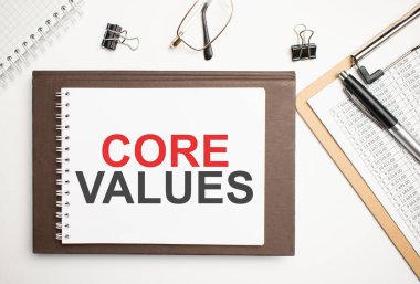Masaüstünde raporlar, not defterleri, hesap makinesi, nakit para ve Core Values yazılı sarı çıkartma var. İş konsepti