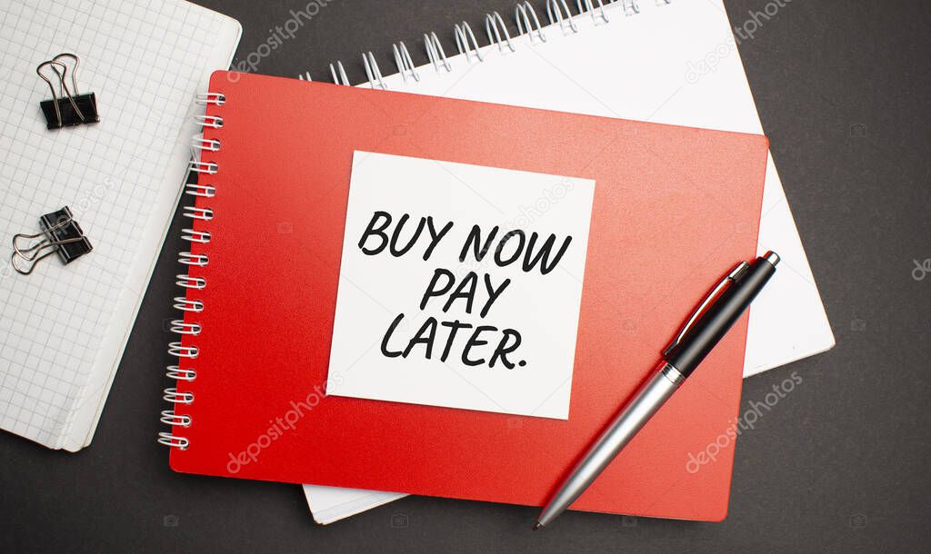 BUY NOW PAY LATER sign on sheet of paper on the red notepad with pen