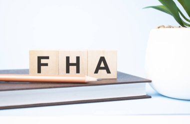 FHA acronym on building blocks supported by two different size pencils. Copy space.