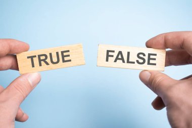 Erkek el iki tahta kazık tutuyor, birinde gerçek, diğerinde sahte işareti var..