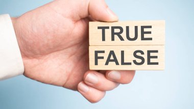 Erkek el iki tahta kazık tutuyor, birinde gerçek, diğerinde sahte işareti var..