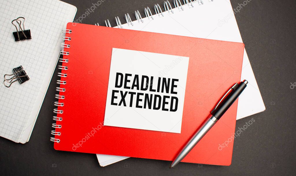 DEADLINE EXTENDED sign on sheet of paper on the red notepad with pen