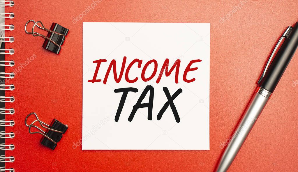 INCOME TAX sign on sheet of paper on the red notepad with pen