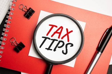 Masaüstünde raporlar, not defterleri, bir hesap makinesi, bir nakit para ve TAX TIPS yazılı sarı bir çıkartma var. İş konsepti