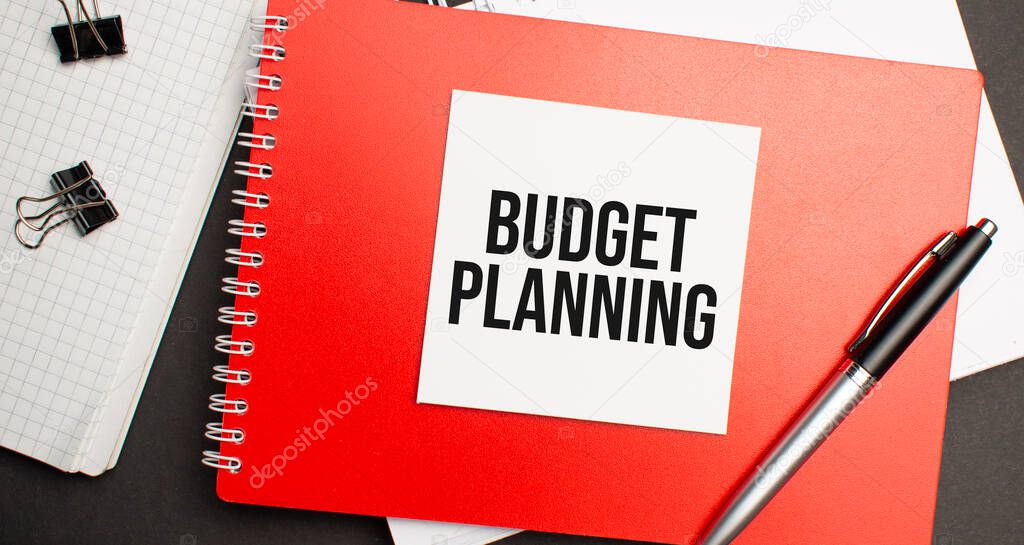 BUDGET PLANNING sign on sheet of paper on the red notepad with pen