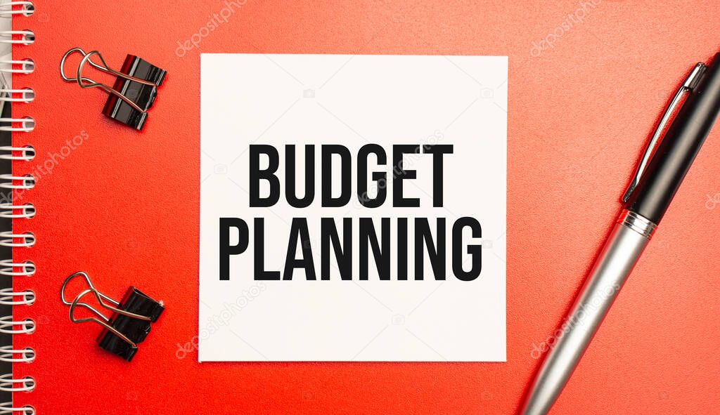 BUDGET PLANNING sign on sheet of paper on the red notepad with pen